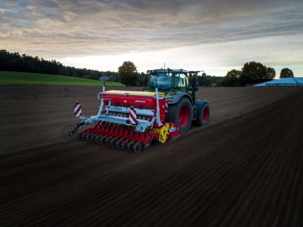 Traktor mit Saatmaschine bearbeitet ein Feld unter bewölktem Himmel.